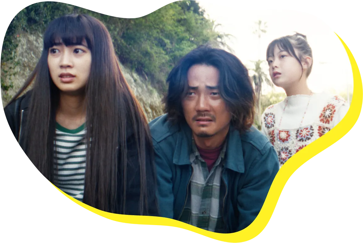 映画の場面。父と二人の娘が並んで前方を見つめる